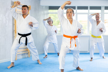 Diligent old man attendee of karate classes practicing kata standing in row with others in sports...