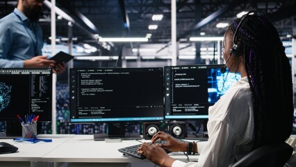 Obraz premium Admin in data center wearing headset assisting users with artificial intelligence troubleshooting. African american woman in server room hub managing support tickets using automated systems, camera A