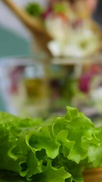 Woman's hands mixing a fresh vegetarian salad in a glass bowl with wooden spoons. Delicious and healthy food prepared with organic ingredients in a bright and cozy home kitchen