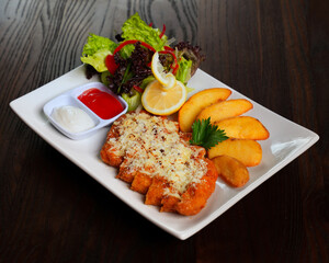 Chicken Schnitzel with Cheese, Potato Wedges, and Fresh Salad Served on White Plate