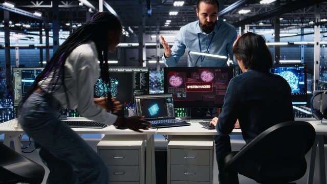Server hub engineers alarmed by cyberattack accessing confidential data, working to secure systems. Teamworking data center colleagues fighting malware intrusion during security breach, camera A