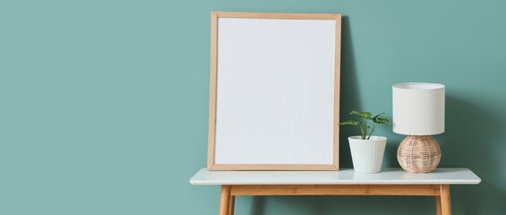 Lamp with plant and frame on table near light blue wall. Banner for design