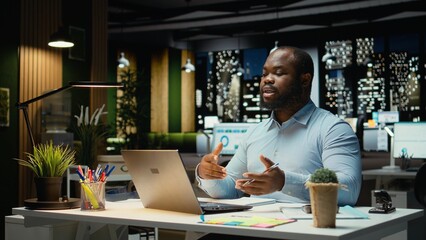 African american worker attends a remote web discussion with associates on telework call, participating in a meeting via telephone from office at night. Employee negotiating with board.