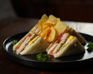 Club Sandwich with Ham, Egg, and Vegetables Served with Potato Chips on Black Plate