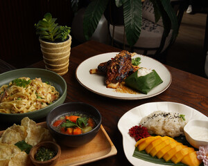 Assorted Indonesian Dishes with Mango Sticky Rice and Traditional Side Dishes on Wooden Table