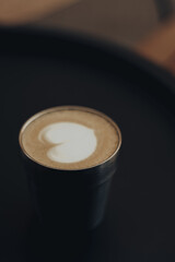 Minimalist coffee aesthetic with creamy latte art in a stylish metal cup on a dark background. Warm tones, soft focus and elegant composition create a cozy, modern cafe vibe. Coffee shop. Hot drink.