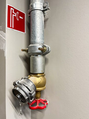 Industrial fire safety equipment featuring a metallic pipe with a valve and a red handle, mounted on a wall, alongside a fire exit sign for emergency preparedness