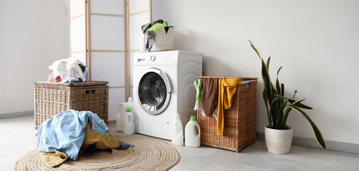 Interior of light bathroom with washing machine, pile of dirty clothes and laundry basket