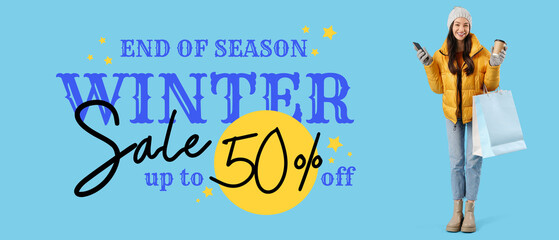 Young woman in winter clothes with shopping bags, coffee and mobile phone on blue background