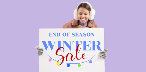 Young woman in warm earmuffs with blank poster on lilac background