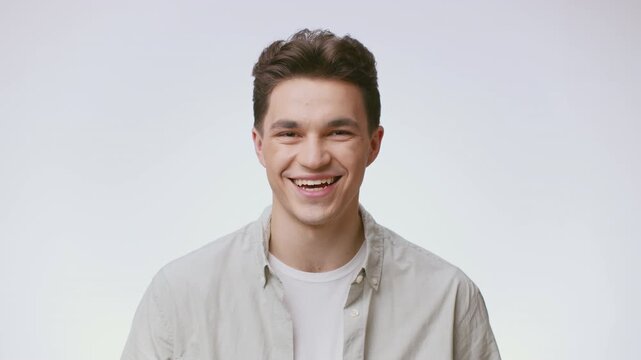 A young man stands confidently against a plain backdrop, showcasing his charming smile and casual style. He embodies a modern lifestyle relevant to Gen Z.