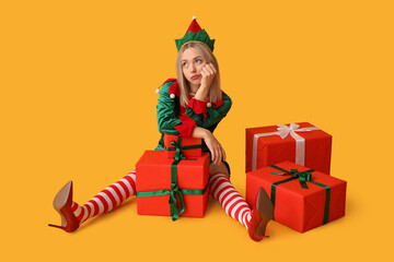 Young woman in elf costume with Christmas gift boxes on yellow background