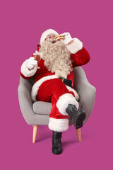 Santa Claus with glass of beer and tasty burger in armchair on purple background