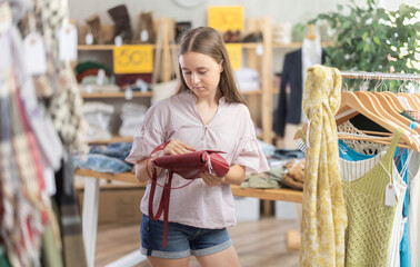 Teen girl buyer choosing handbag in clothing store