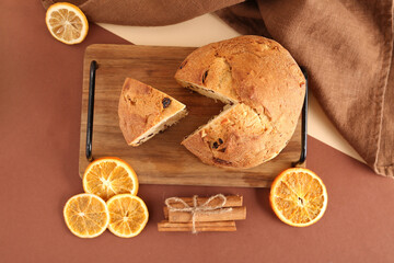 Wooden tray with tasty Panettone, slices of dried orange and cinnamon sticks on colorful background