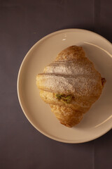 A beautifully crafted croissant is elegantly displayed on a plate, dusted generously with powdered sugar