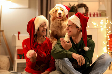 Happy young couple with dog in Santa hats at home on Christmas eve