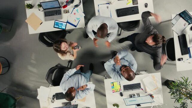 Top down view zoom in of staff proud of their successful teamwork collaboration, clapping hands after analysis. Employees use data visualization and forecasting for project objectives. Camera A.