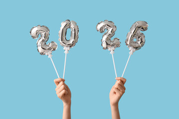 Female hands with figure 2025 made of foil balloons on blue background