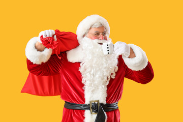 Santa Claus with Christmas bag and cup of cacao on yellow background