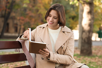 Obraz premium Beautiful young happy woman reading book on bench in autumn park