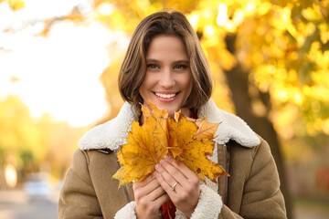 Beautiful young happy woman with fall leaves in autumn park