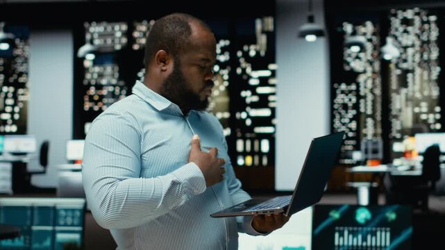 Black guy examining archived documents before transcribing on pc notebook, notetaking and extracting the main points from reports on laptop. Analyst documenting after hours late at night. Camera B.