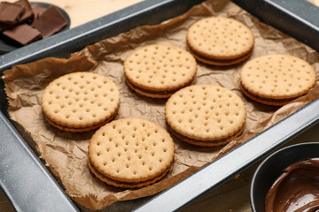 Baking dish with tasty sandwich biscuits and bowl of chocolate cream, closeup