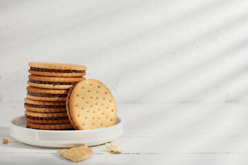 Plate with stack of tasty sandwich biscuits on white wooden table