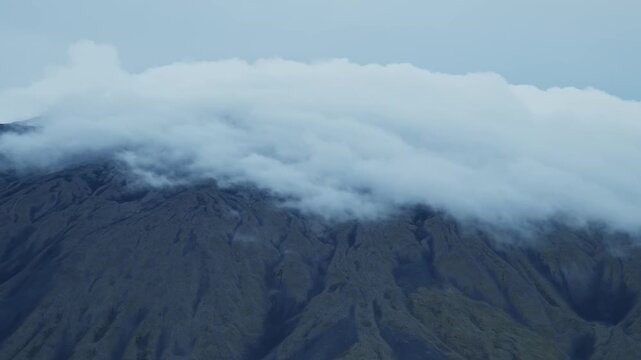 A scenic shot of a rocky mountain range with a dense band of clouds covering the upper slopes and peaks. The overcast sky creates a moody and dramatic atmosphere, perfect for projects related to natur