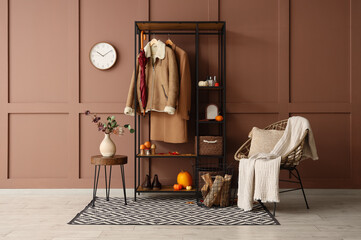 Armchair, rack with clothes and pumpkins in interior of hallway