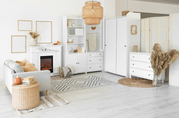 Interior of living room with grey sofa, coffee table, shelving units and autumn home decor on fireplace near white wall