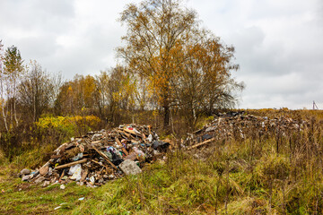 Unsightly heaps of discarded waste and rubble clutter an autumn field, a bleak human impact on nature under a gray, overcast sky, highlighting pollution