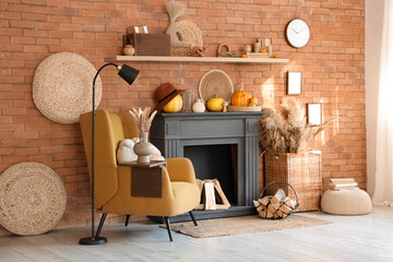 Naklejka premium Interior of living room with armchair, lamp, pumpkins and autumn home decor on fireplace near brick wall