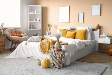 Interior of modern bedroom with comfortable bed, table, shelving unit and pumpkins near window