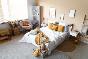 Interior of modern bedroom with comfortable bed, table, shelving unit and pumpkins
