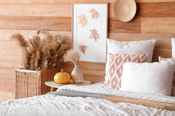 Comfortable bed, table and wicker basket with pampas grass in interior of bedroom