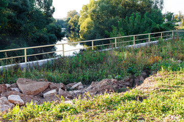 River slope erosion control with concrete rubble and dirt. A sturdy railing overlooks the river winding through lush trees