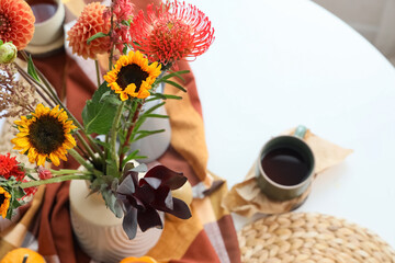 Vase with autumn flowers on dining table in room, closeup