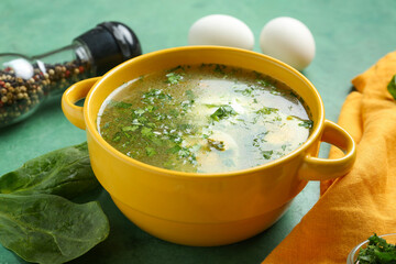 Pot of tasty green borscht with spinach leaves on green grunge background
