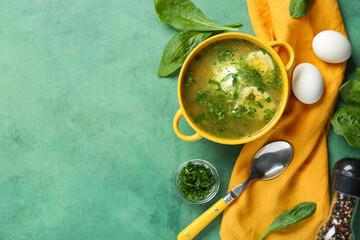 Pot of tasty green borscht with eggs, peppercorns, spinach leaves and spoon on green grunge background