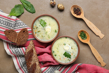 Bowls of tasty green borscht with eggs, spinach leaves, peppercorns, greens and baguette on brown grunge background