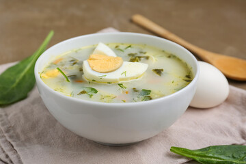 Bowl of tasty green borscht with eggs, spinach leaves and wooden spoon on brown grunge background