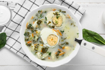 Bowl of tasty green borscht with spinach leaves and sour cream on white wooden background