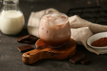 Glass of cold cocoa drink and jug of fresh milk on black background, closeup