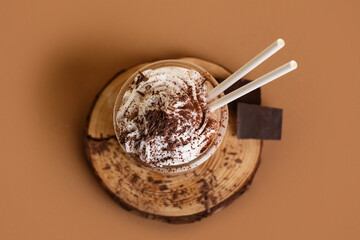 Glass of cold cocoa drink with whipped cream and chocolate on brown background
