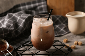 Glass of cold cocoa drink and jug of fresh milk on grey background