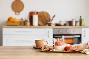 Burning candles, autumn decor and cup of tea on table in interior of kitchen, closeup