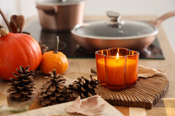 Burning candle, pumpkins and fir cones on table in kitchen, closeup