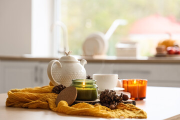 Teapot, cup of tea, autumn decor and burning candles on table in kitchen, closeup
